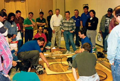 Gene Klotz (blue shirt at left) and Chuck Crispin (blue shirt at right) do a demo at the first National Wood Flooring Association Advanced School in January 1995.