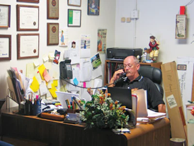 Surrounded at his desk by company awards, NWFA certifications, a collection of sticky notes and golf paraphernalia, Williford discusses a supply order delivery.