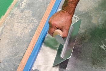 photo of someone gluing down flooring to backer a board
