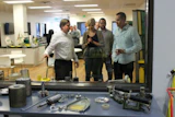 Palo Duro Hardwoods Vice President of Sales Tom Ruekert shows visitors at Lägler's recent grand opening a display of new Lägler sanding machine parts. On the table in the foreground are used parts in the company's Premium Sanding Training area. The worn parts are used to help training participants understand proper machine usage and wear.