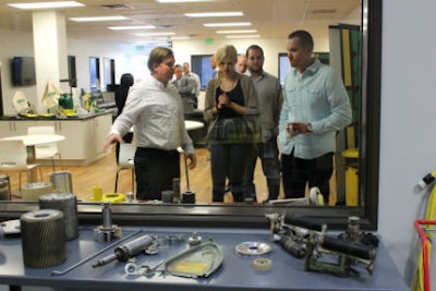 Palo Duro Hardwoods Vice President of Sales Tom Ruekert shows visitors at Lägler's recent grand opening a display of new Lägler sanding machine parts. On the table in the foreground are used parts in the company's Premium Sanding Training area. The worn parts are used to help training participants understand proper machine usage and wear.