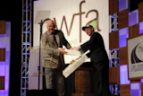 Incoming NWFA Chairman Tommy Maxwell of Maxwell Hardwood Flooring gives Immediate Past Chairman Jeff Fairbanks of Palo Duro Hardwoods a Ricky Bobby costume on stage during the General Session at Expo 2016.