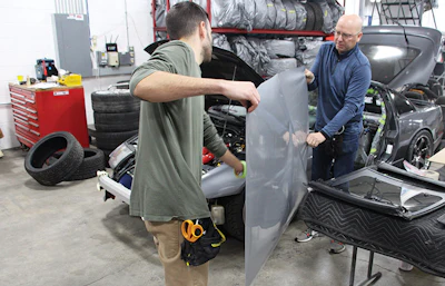 Parker and Hagen prepare to fit a satin gray vinyl wrap over the front of a vehicle.