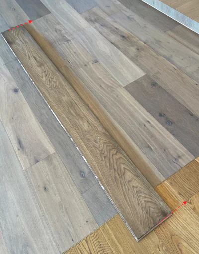 An important part of our 'Scribed Flow-Through' technique is that the boards are the factory (long) lengths, meaning we carry the appearance of original lengths throughout the floor even when the color changes or the surface angle changes—it's like the board just changes colors. The board on top here shows what the factory length is and how that length is carried through in the installed floor even over three changes of color or angle. If I make a mistake, generally, I will remove the good parts of the board out of the bed of glue just to maintain our visual flow-through.