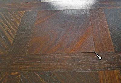 Figure 1: Three-layer parquet with smoked-oak top layer, bonded to a heated screed and with oiled surface. The grain is diagonal to the panel edges. The direction of maximum swelling and shrinkage, which is perpendicular to this, thus runs exactly between two of the corners. The site visit took place in summer. The users reported that the corner curling was much more pronounced in the heating season.