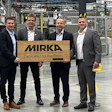 Four business professionals standing in Mirka manufacturing facility with branded wooden sign