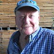 Smiling senior man in blue plaid shirt and baseball cap against wooden background