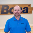 Smiling employee in blue Bona polo shirt standing in front of company logo