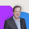 Professional man in gray suit smiling, with purple and blue geometric background