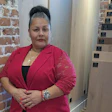 Professional woman in red blazer standing by brick wall with wooden panels