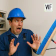 Electrician in blue hard hat looking shocked near electrical panel and blue broom