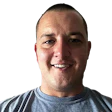 Smiling man in gray shirt with buzzed hair looking directly at camera
