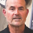 Middle-aged bald man with gray beard in black shirt looking directly at camera