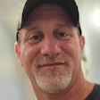 Middle-aged man with gray beard smiling, wearing black baseball cap