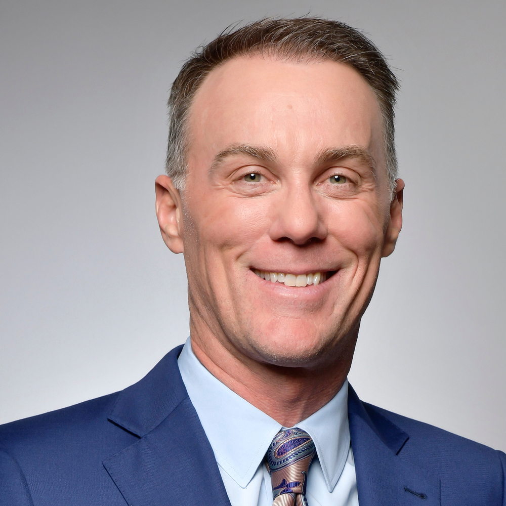 Smiling professional in blue suit and patterned tie against neutral background