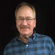 Middle-aged man wearing glasses and blue plaid shirt smiling at camera