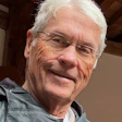 Older man with white hair and glasses smiling at camera indoors