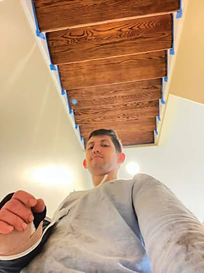 Man looking down at camera beneath wooden ceiling panels with blue painter's tape during renovation
