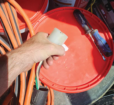 Worker holding paint brush over red bucket with tools and orange extension cords on construction site