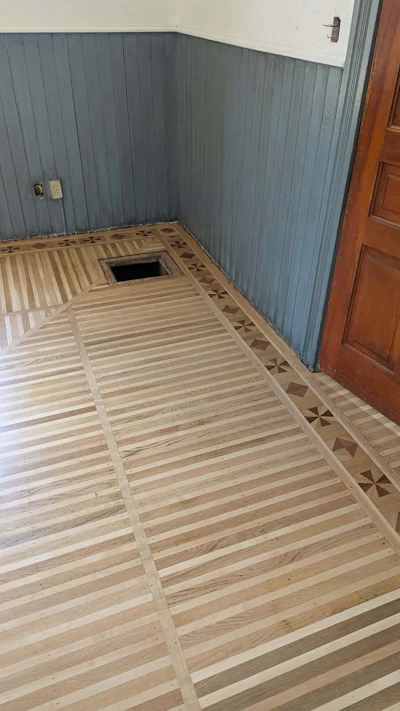 Interior room with light wood flooring, decorative border inlay, and gray beadboard wall paneling during renovation