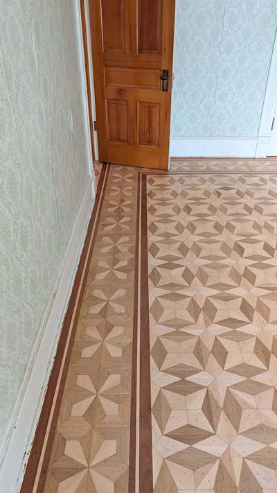 Hallway with geometric parquet flooring, patterned wallpaper, and wooden six-panel door