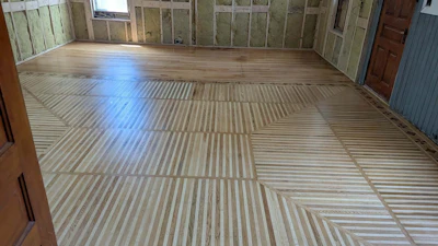 Spacious room with geometric wood flooring featuring herringbone and linear patterns, natural light from windows, and paneled walls.