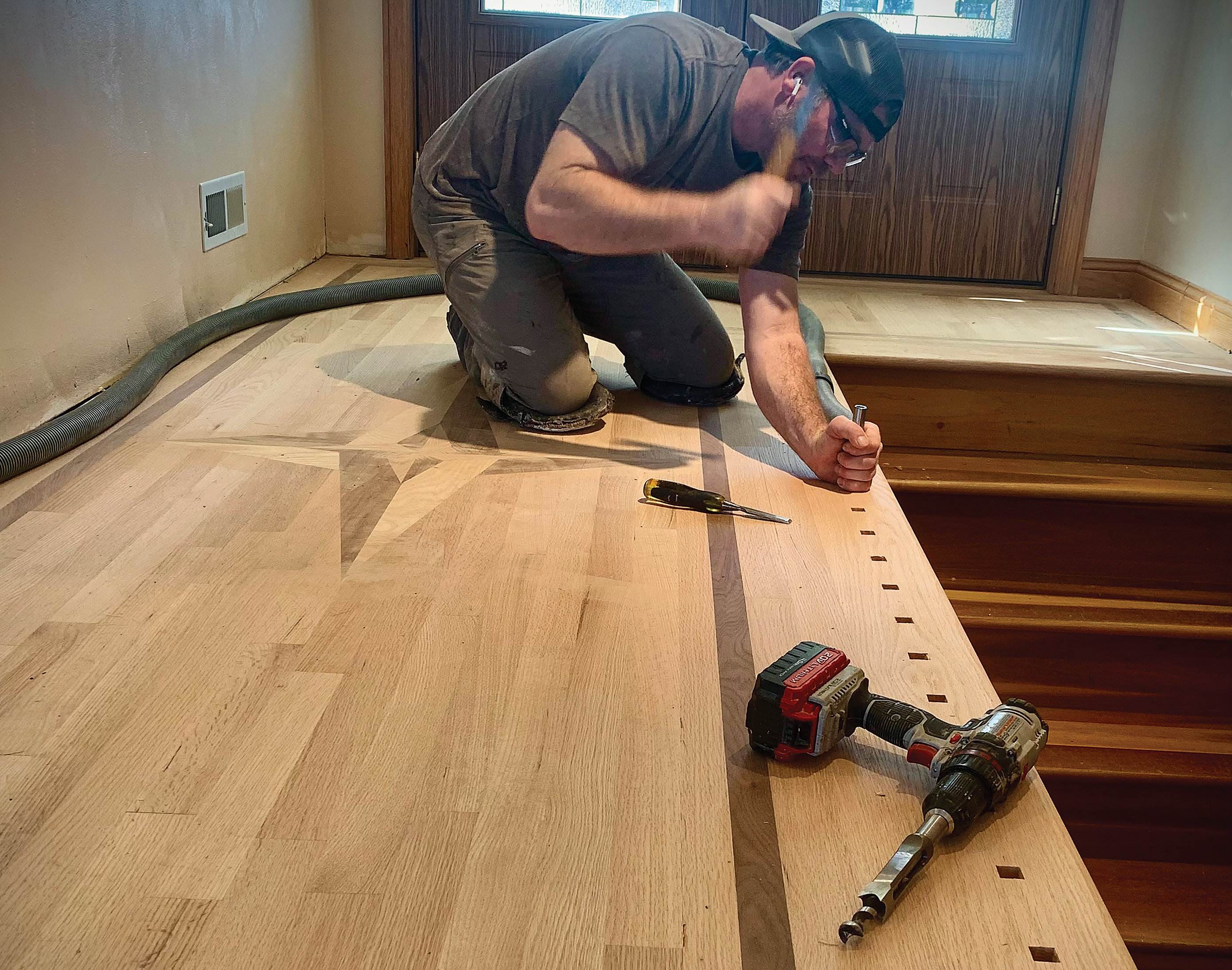 Carpenter installing hardwood flooring with power drill in residential room