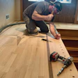 Carpenter installing hardwood flooring with power drill in residential room