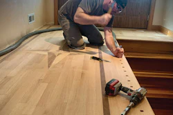 Carpenter installing hardwood flooring with power drill in residential room