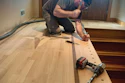 Carpenter installing hardwood flooring with power drill in residential room