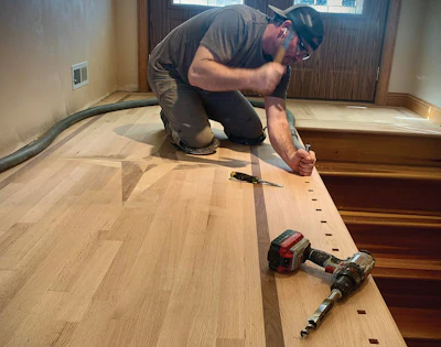 Carpenter installing hardwood flooring with power drill in residential room