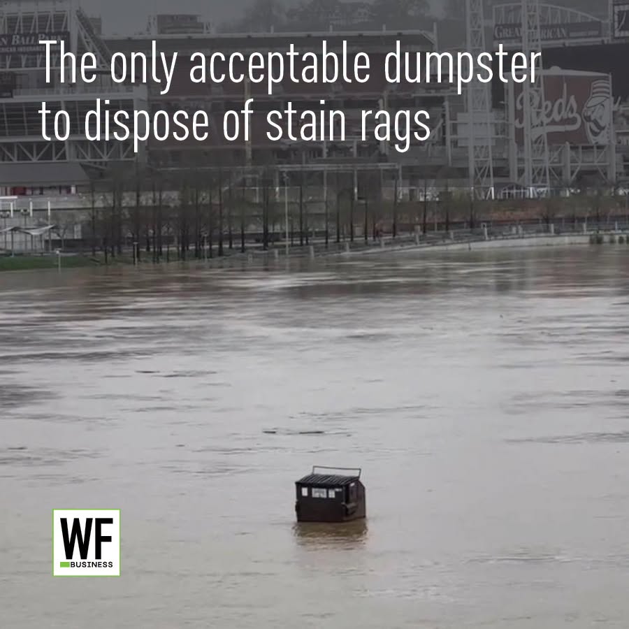 Dumpster partially submerged in floodwater at urban waterfront with stadium in background