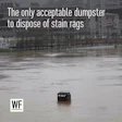 Dumpster partially submerged in floodwater at urban waterfront with stadium in background