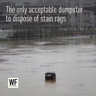 Dumpster partially submerged in floodwater at urban waterfront with stadium in background