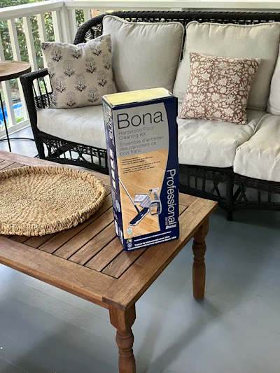 Bona Hardwood Cleaning Kit displayed on wooden coffee table in sunroom with wicker pet bed and black wicker chair with cushions