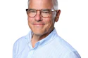 Professional headshot of middle-aged man wearing light blue pinstriped shirt and glasses
