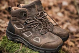 Pair of brown suede hiking boots with black soles positioned on moss and rocky terrain