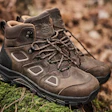 Pair of brown suede hiking boots with black soles positioned on moss and rocky terrain