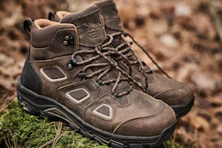 Pair of brown suede hiking boots with black soles positioned on moss and rocky terrain