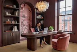 Modern burgundy office with arched shelving, wooden desk, pink velvet chair, glass chandelier, and city views