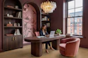 Modern burgundy office with arched shelving, wooden desk, pink velvet chair, glass chandelier, and city views