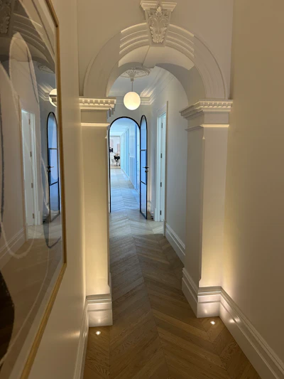 Elegant hallway with barrel vault ceiling, ornate capitals, and arched doorways lit by warm ambient lighting
