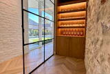 Modern entryway with black-framed glass doors, white brick walls, chevron flooring, and illuminated wooden wine display cabinet