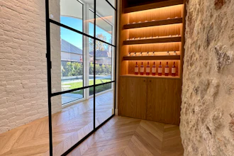 Modern entryway with black-framed glass doors, white brick walls, chevron flooring, and illuminated wooden wine display cabinet