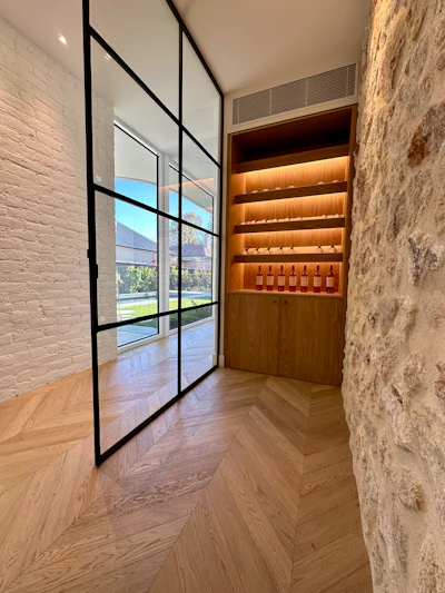 Modern entryway with black-framed glass doors, white brick walls, chevron flooring, and illuminated wooden wine display cabinet