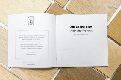 PID Floors children's book spread showing title 'Out of the City, Into the Forest' with company logo and dedication page