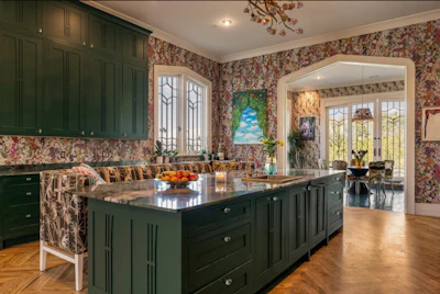 Elegant kitchen with dark green cabinetry, floral wallpaper, black island countertop, and French doors opening to adjoining room