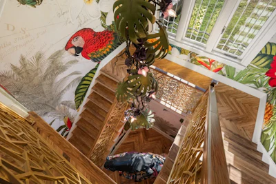 Overhead view of wooden staircase with tropical-themed wallpaper ceiling featuring red macaw and green foliage