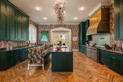 Luxury kitchen with dark green cabinetry, floral wallpaper, herringbone wood flooring, and professional stainless steel appliances